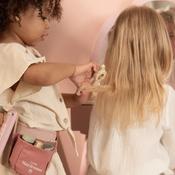 Two children playing with a hairdresser's set in a pink-themed room.